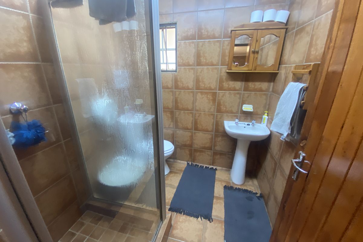 A compact bathroom featuring a shower enclosure, pedestal basin, and toilet, finished with dated brown wall and floor tiles.