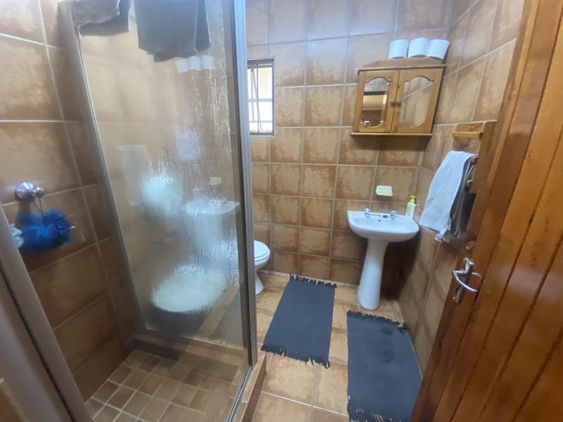A compact bathroom featuring a shower enclosure, pedestal basin, and toilet, finished with dated brown wall and floor tiles.