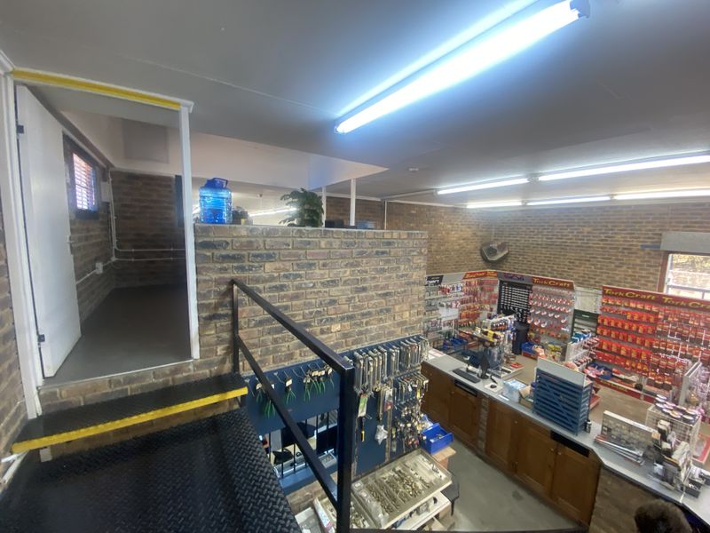 A retail space featuring exposed brick walls, fluorescent lighting, and a metal staircase leading to an upper level with a service counter area.