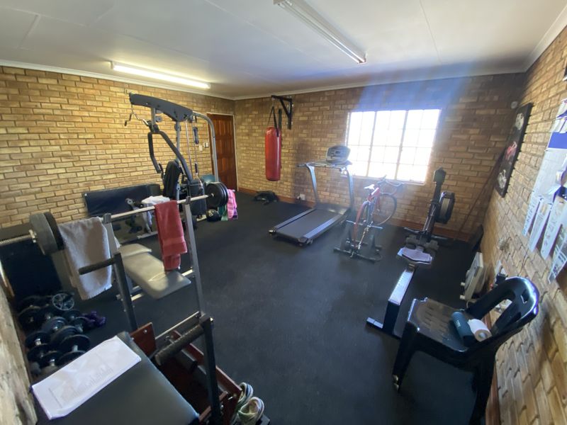 A dedicated home gym space featuring exposed brick walls, durable rubber flooring, and functional overhead lighting, currently equipped with various fitness equipment.