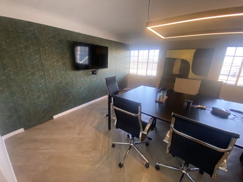 A modern office space featuring herringbone flooring, contemporary lighting, and window shutters, suitable for a professional meeting or workspace environment.
