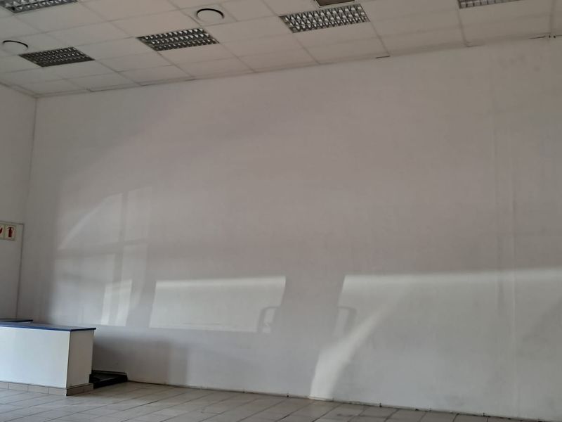An empty retail space featuring a suspended ceiling with recessed lighting, tiled flooring, and a built-in service counter.