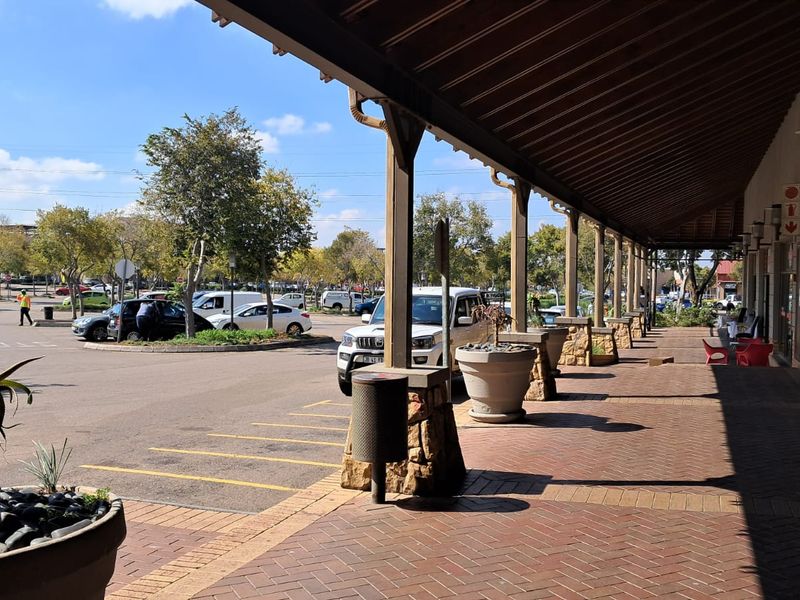 A well-maintained retail storefront featuring a covered brick-paved walkway, stone-clad support pillars, and large glass display windows overlooking a parking area.