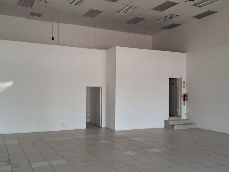 A spacious, vacant retail unit featuring tiled flooring, a suspended ceiling with recessed lighting, and two separate internal access points.