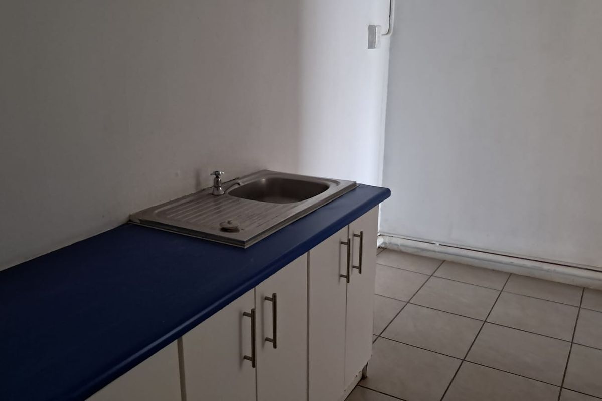 A compact, empty kitchen area featuring a stainless steel sink, blue laminate countertop, white base cabinetry, and neutral ceramic floor tiles.