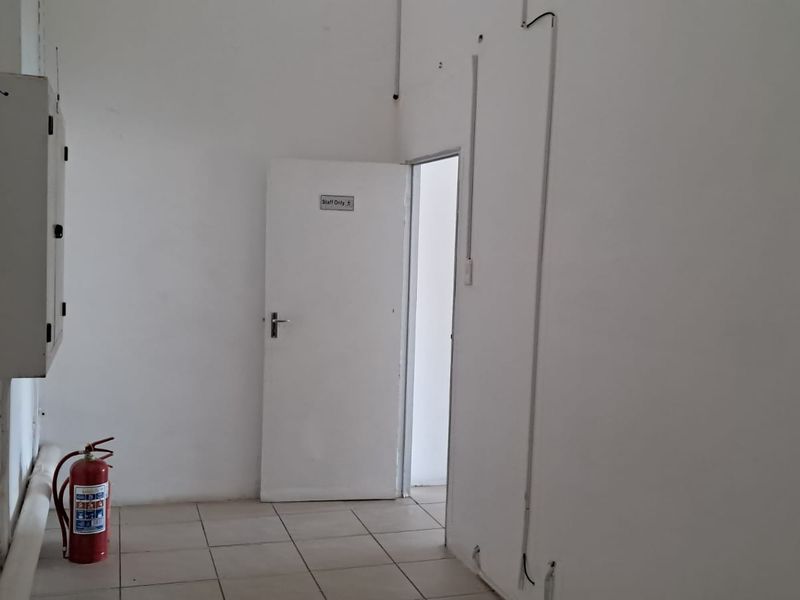 A functional utility space featuring tiled flooring, an electrical distribution board, and a fire extinguisher, providing access to a staff-only area.