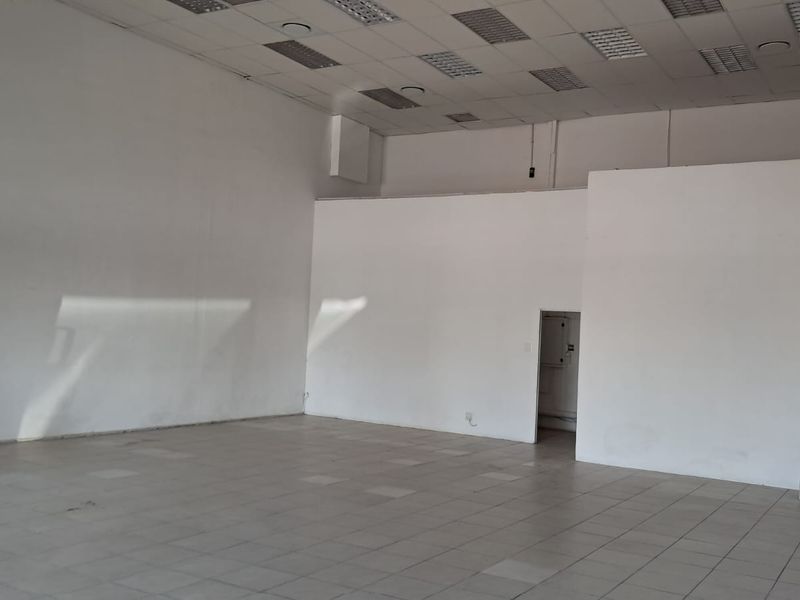 A spacious, empty retail unit featuring tiled flooring, a suspended ceiling with recessed lighting, and neutral white walls, suitable for various commercial business applications.