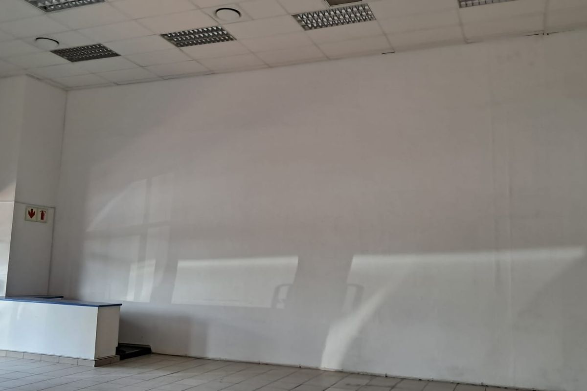 An empty retail space featuring a suspended ceiling with recessed lighting, tiled flooring, and a built-in service counter.