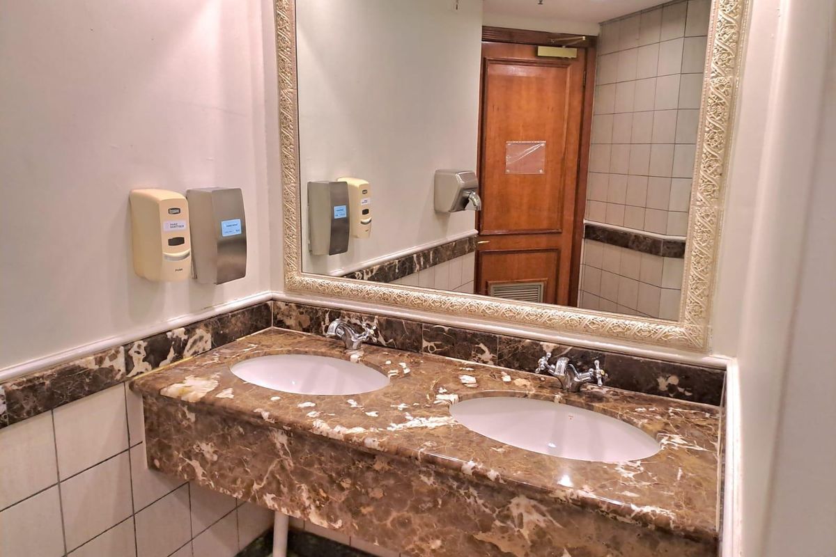 A commercial office bathroom featuring a double vanity with marble countertop, integrated sinks, and wall-mounted soap dispensers.