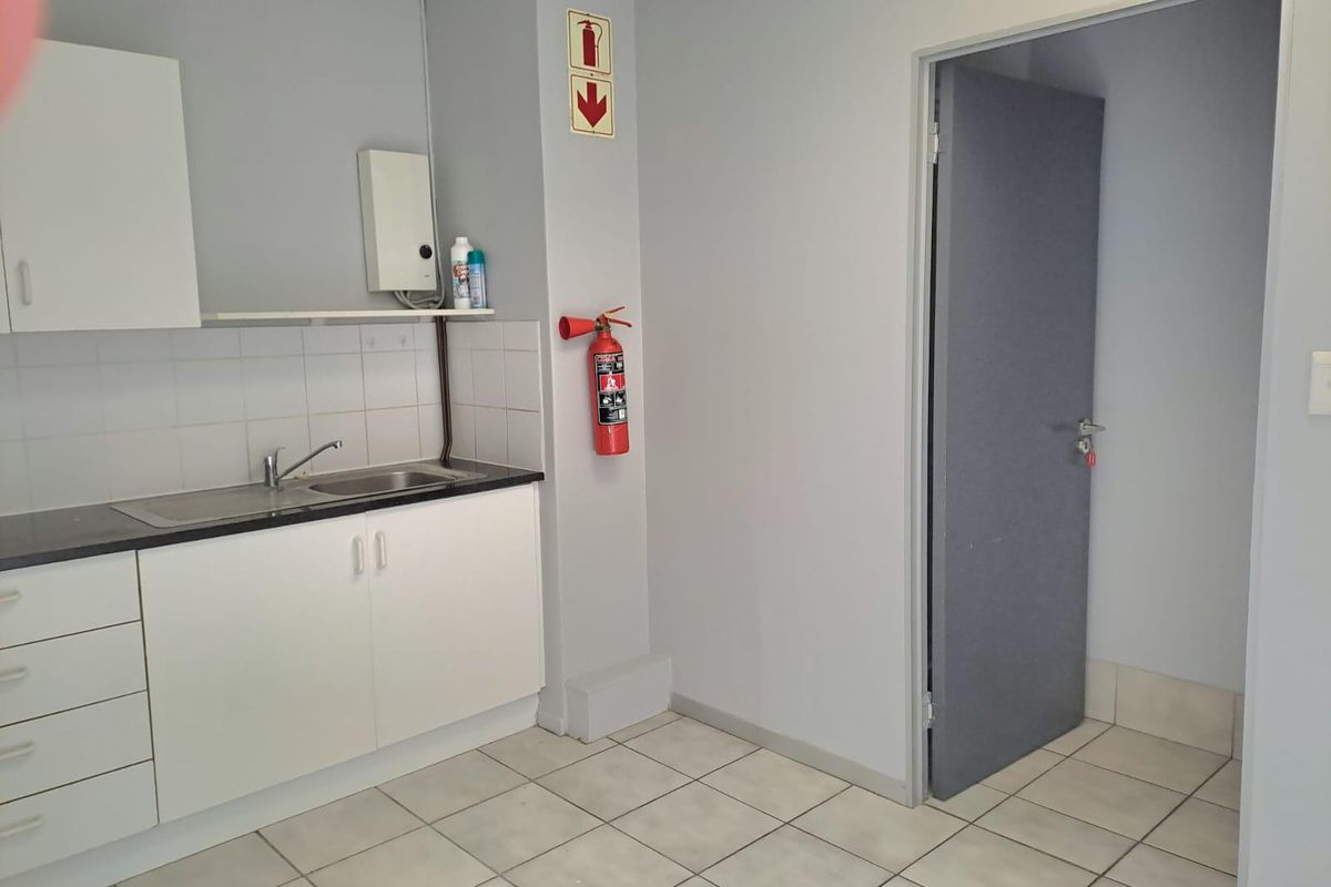 A functional office kitchenette featuring white cabinetry, a stainless steel sink, tiled backsplash, and essential fire safety equipment.