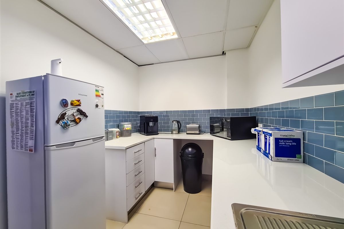 A functional office kitchenette featuring white cabinetry, stone-look countertops, blue subway tile backsplash, and a recessed ceiling light panel.