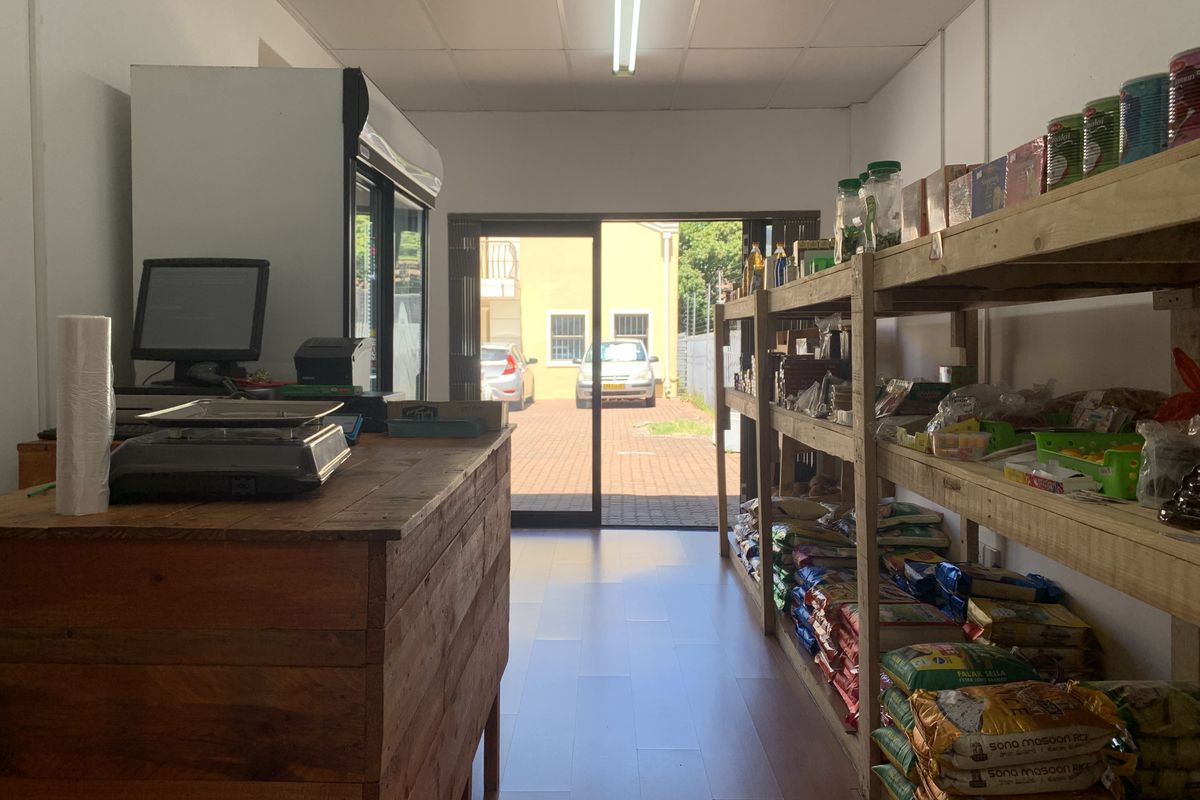 Commercial retail space featuring a service counter, wooden shelving units, and sliding glass doors leading to an exterior parking area.