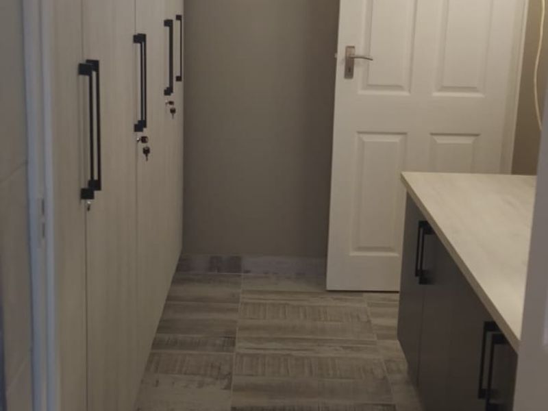A clean, modern scullery or utility space featuring extensive built-in cabinetry, a laminate countertop, and neutral tiled flooring with a high-level window.