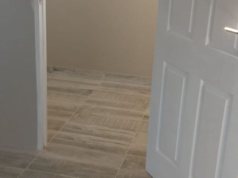A clean, empty hallway featuring modern wood-look tiled flooring and a white internal door leading into an adjacent room.