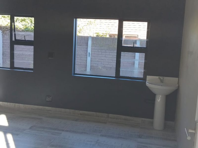 A bright, empty office space featuring modern grey walls, tiled flooring, and a convenient built-in pedestal washbasin.