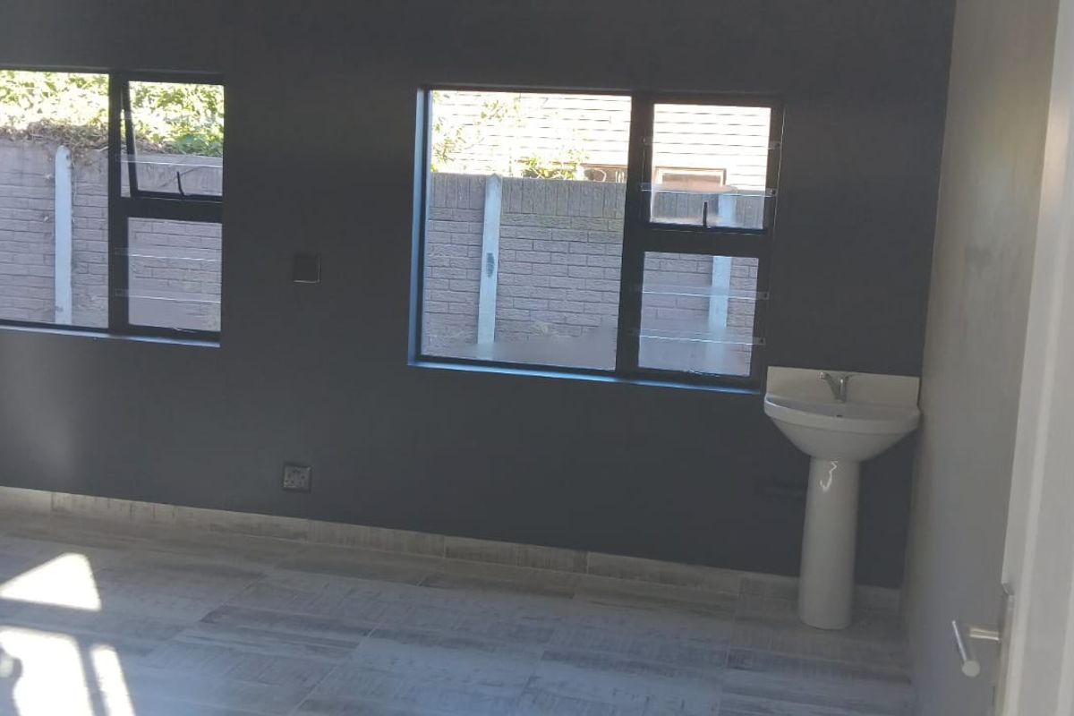 A bright, empty office space featuring modern grey walls, tiled flooring, and a convenient built-in pedestal washbasin.