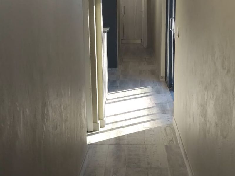 A bright, empty hallway featuring modern wood-look tiled flooring, neutral wall finishes, and recessed ceiling detailing leading toward built-in storage.