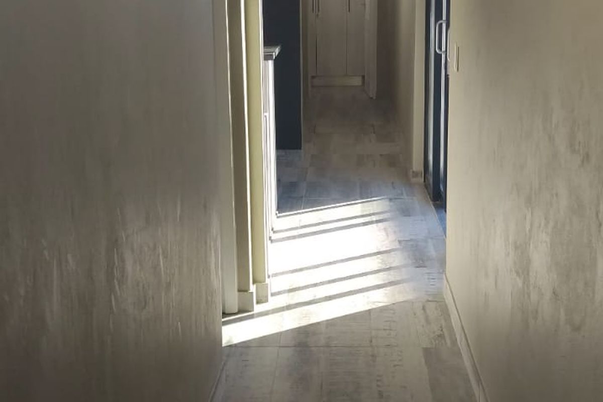 A bright, empty hallway featuring modern wood-look tiled flooring, neutral wall finishes, and recessed ceiling detailing leading toward built-in storage.