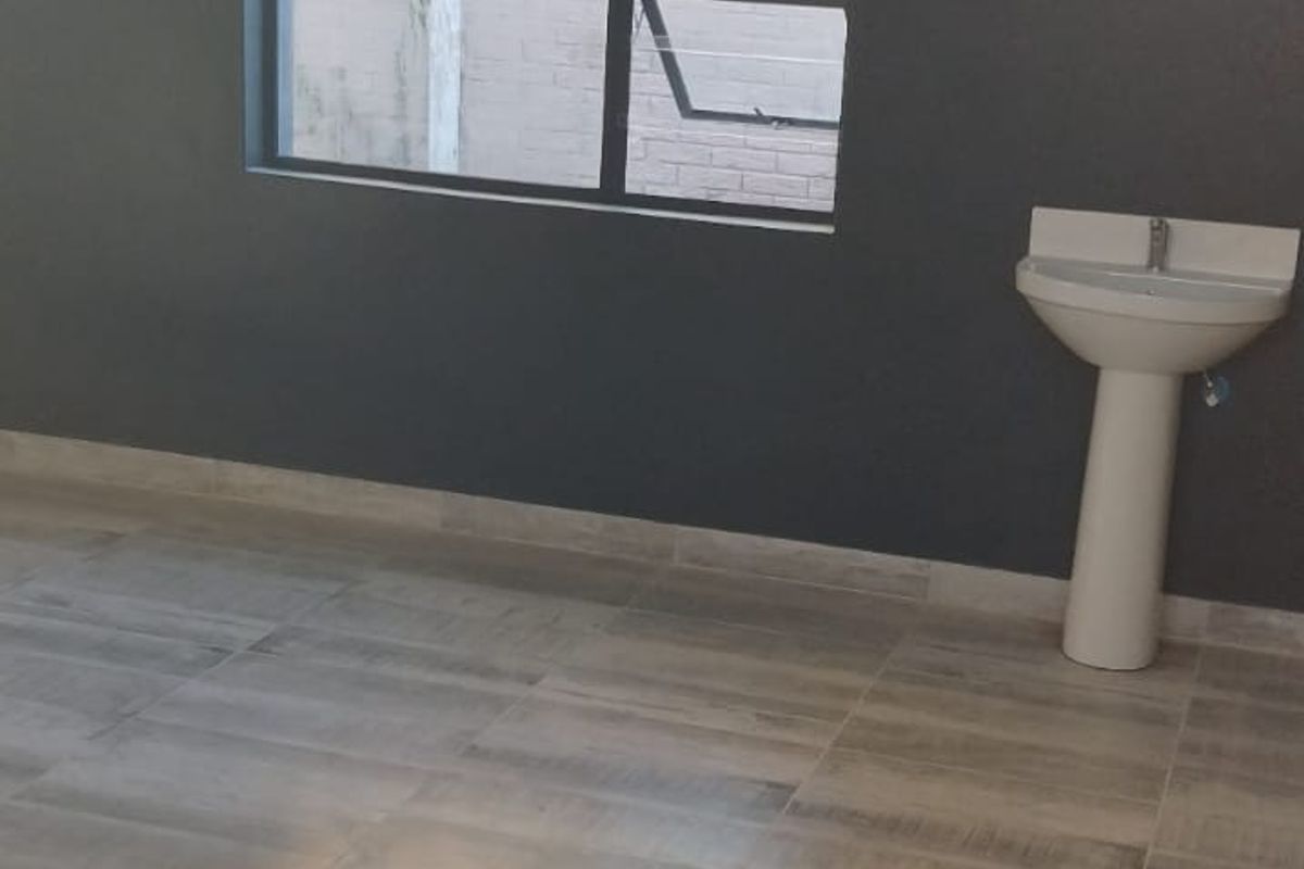 A clean, empty utility space featuring modern grey floor tiles, a pedestal basin, and a dark accent wall with an aluminium window.
