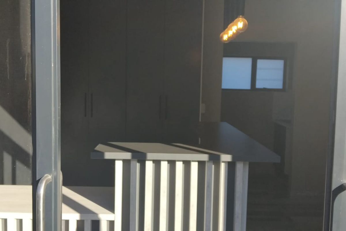 A modern kitchen area featuring built-in cabinetry, a breakfast bar, and pendant lighting, viewed through sliding glass doors.