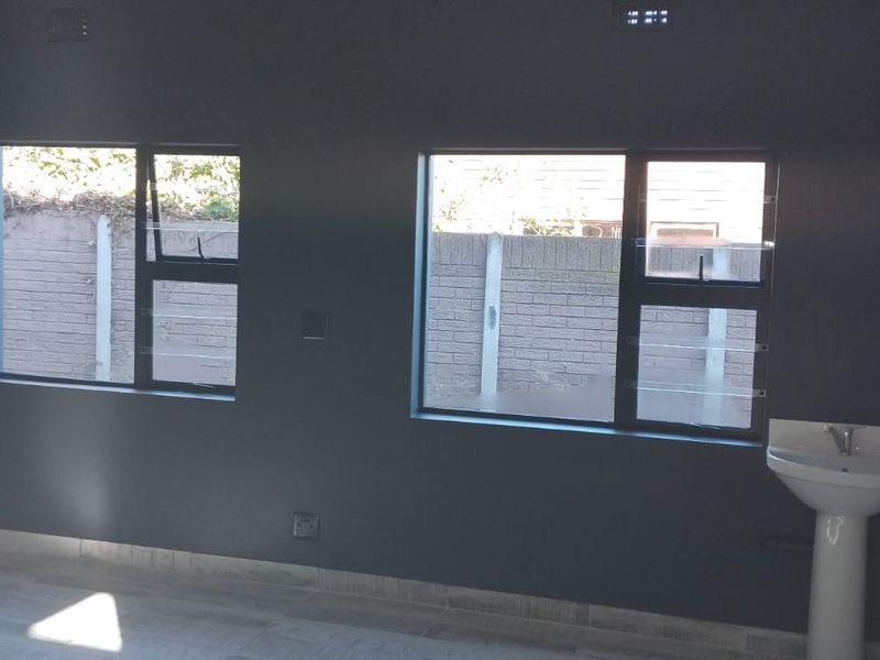 A vacant office space featuring dark accent walls, tiled flooring, and a built-in pedestal washbasin with natural light from aluminium windows.