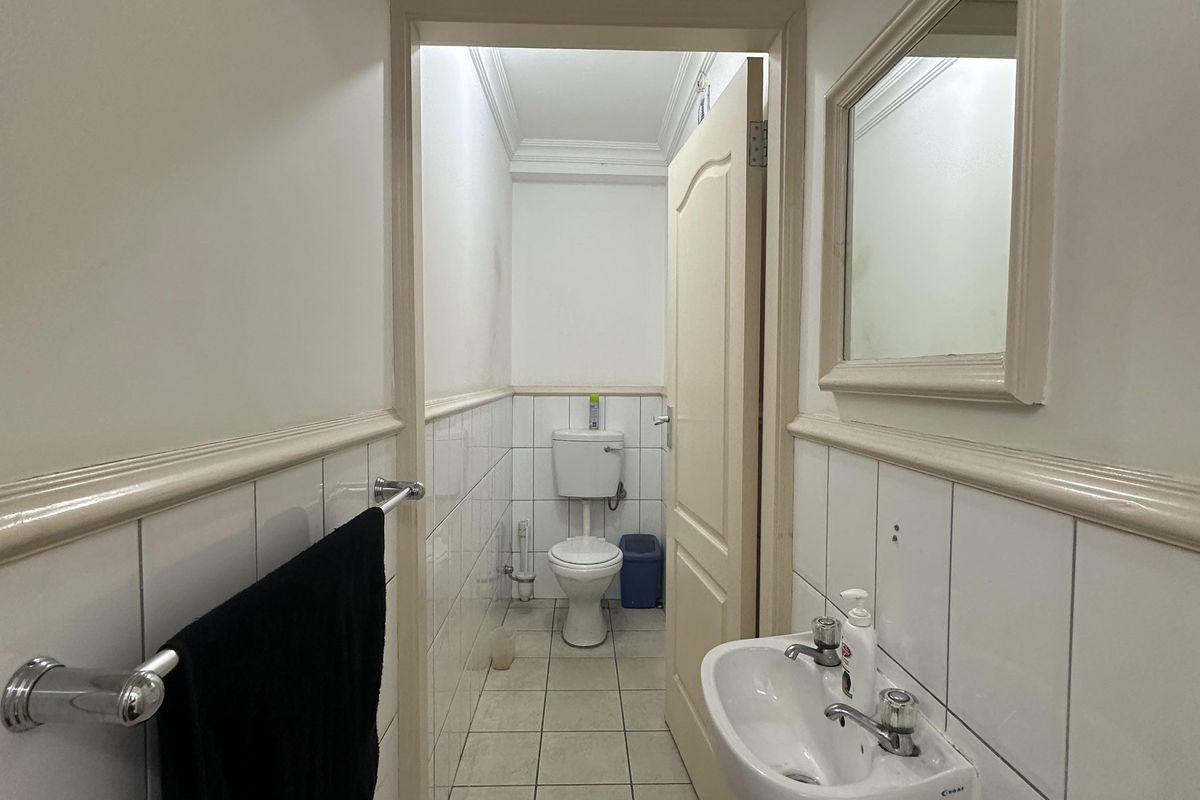 A functional commercial bathroom featuring a wall-mounted basin, tiled walls with dado rail, and a separate toilet cubicle.