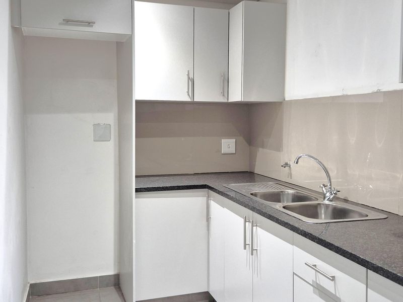 A clean and functional office kitchenette featuring modern white cabinetry, granite countertops, and a double bowl stainless steel sink with a mixer tap.