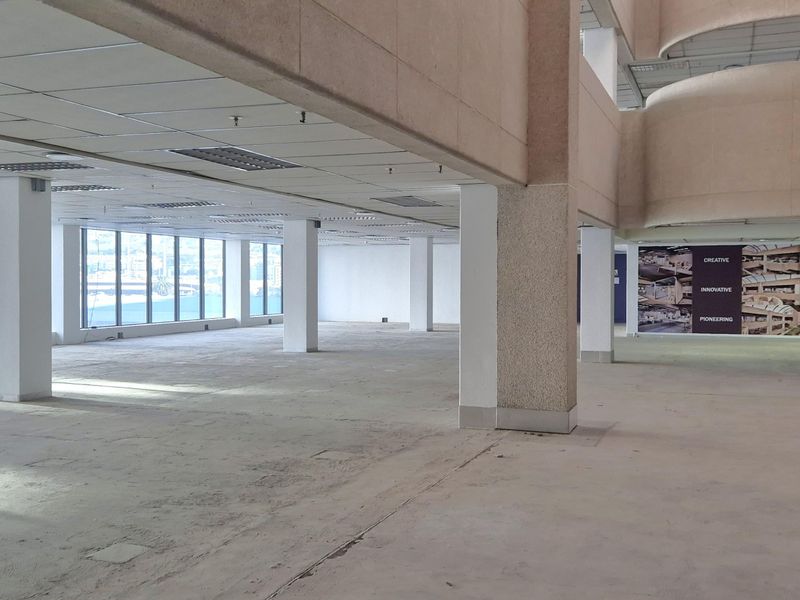 A spacious, open-plan office area featuring large windows, structural columns, and a suspended ceiling, currently vacant and ready for custom fit-out.