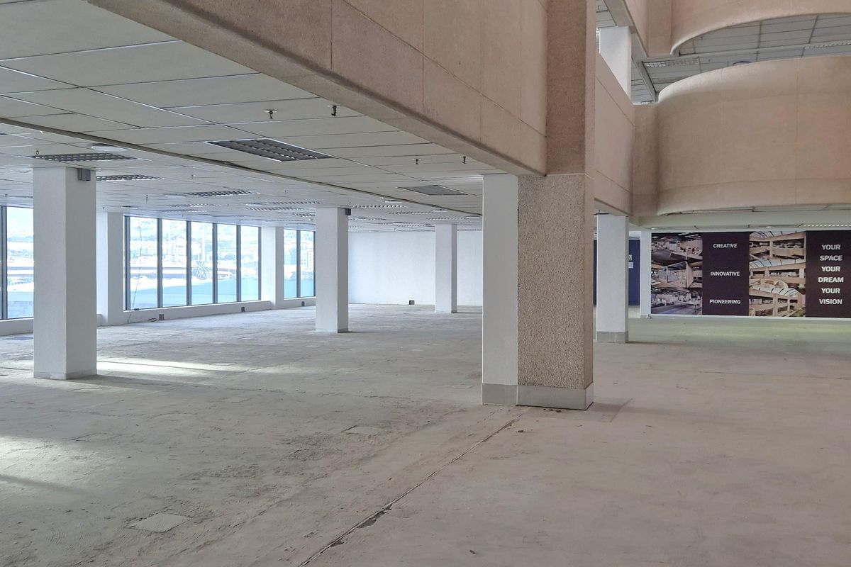 A spacious, open-plan office area featuring large windows, structural columns, and a suspended ceiling, currently vacant and ready for custom fit-out.