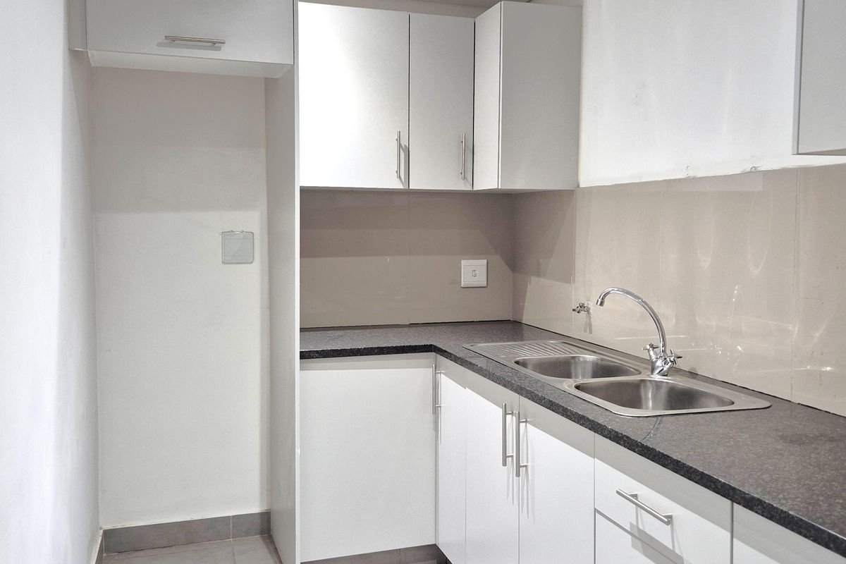 A clean and functional office kitchenette featuring modern white cabinetry, granite countertops, and a double bowl stainless steel sink with a mixer tap.