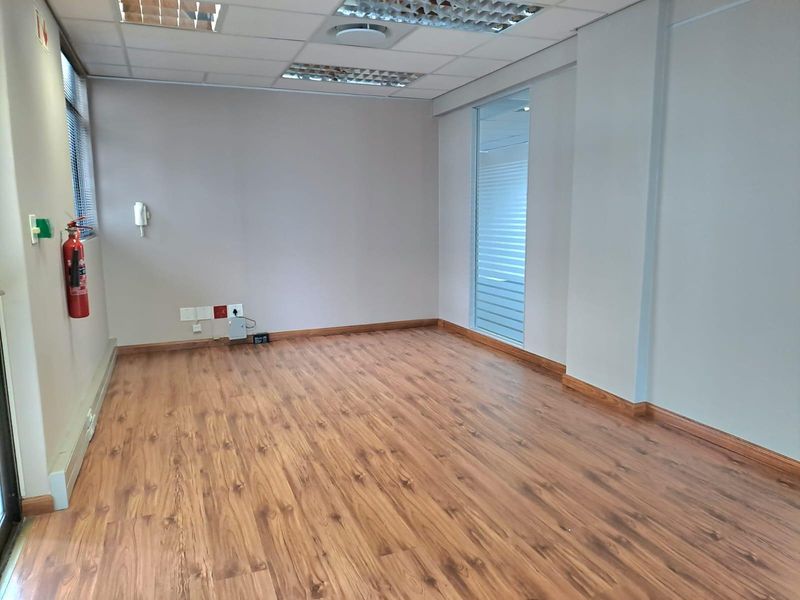 A clean, empty office space featuring laminate wood flooring, a suspended ceiling with recessed lighting, and a glass partition wall.