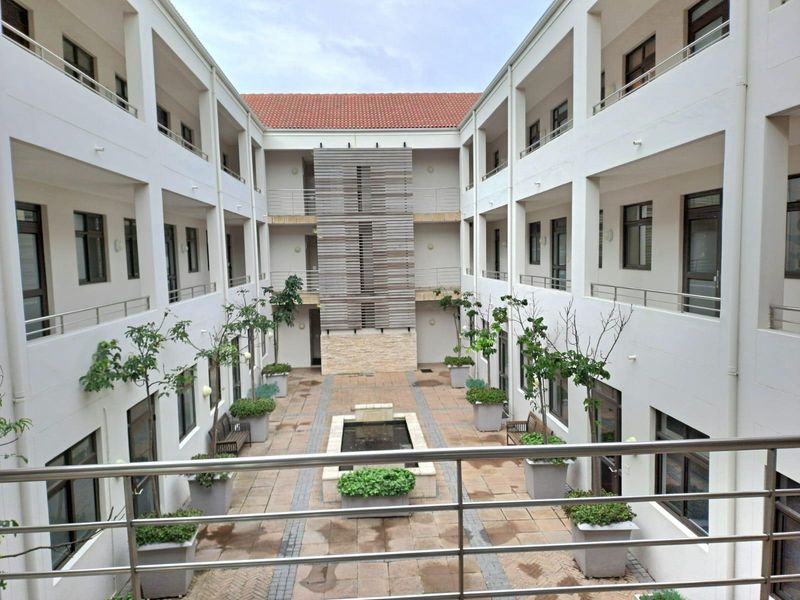 A well-maintained central courtyard within an office complex, featuring stone paving, a central water feature, and multi-level balcony access with stainless steel railings.