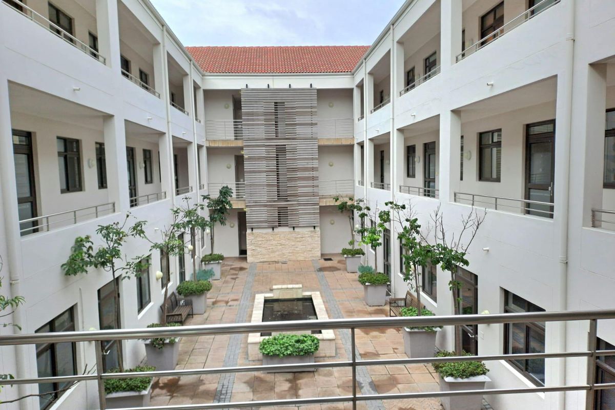 A well-maintained central courtyard within an office complex, featuring stone paving, a central water feature, and multi-level balcony access with stainless steel railings.
