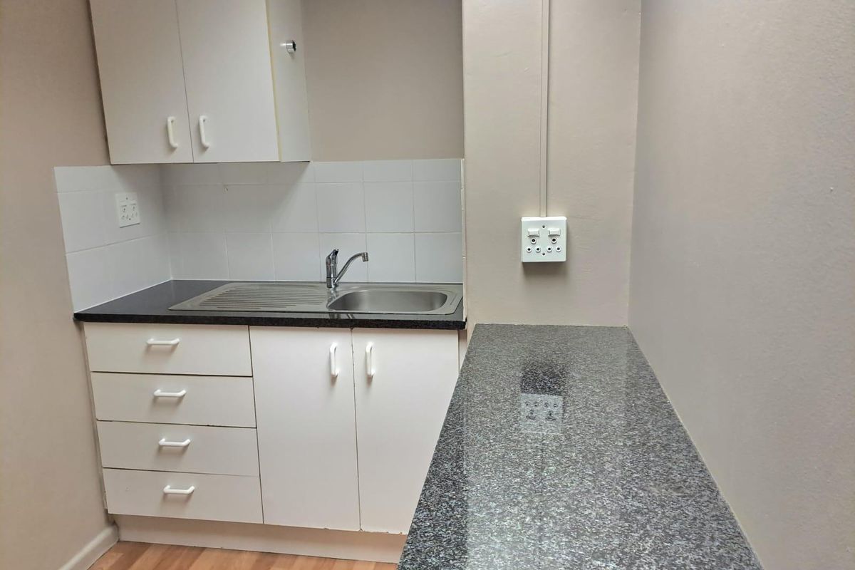 A compact office kitchenette featuring white cabinetry, granite countertops, a stainless steel sink, and a tiled backsplash.