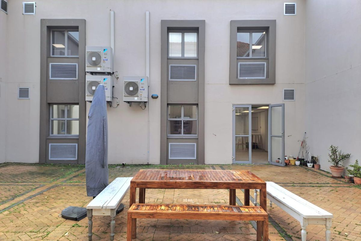 A paved outdoor courtyard area featuring exterior building access, wall-mounted air conditioning units, and integrated ventilation grilles.