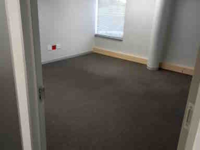 A vacant commercial office space featuring neutral grey walls, carpeted flooring, a structural column, and recessed ceiling lighting.
