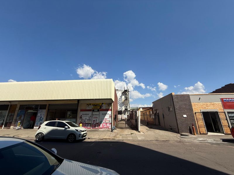 Street-level view of a commercial property featuring metal roller shutter doors, brick facade, and paved access area.