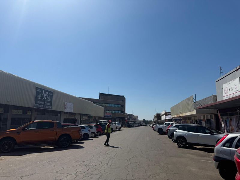 A street-level view of a commercial business district featuring multiple storefronts, metal roofing, and an asphalt road with visible surface cracking.