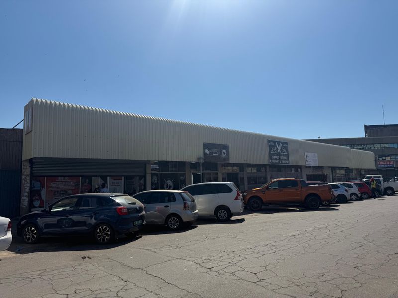 Front elevation of a commercial building featuring corrugated metal roofing and multiple roller shutter access points with an adjacent asphalt parking area.
