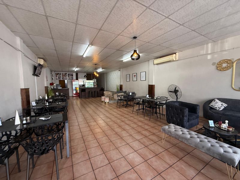 Spacious open-plan commercial dining area featuring tiled flooring, a built-in service counter, and wall-mounted air conditioning units.
