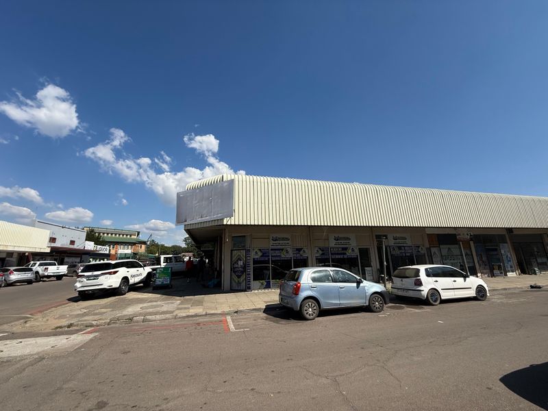 Street-level view of a commercial building featuring a distinctive curved metal roof and multiple shopfront entrances with signage.
