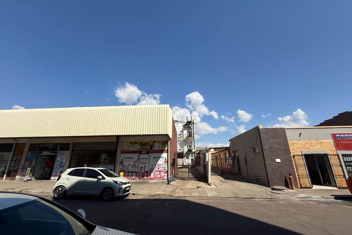 Street-level view of a commercial property featuring metal roller shutter doors, brick facade, and paved access area.