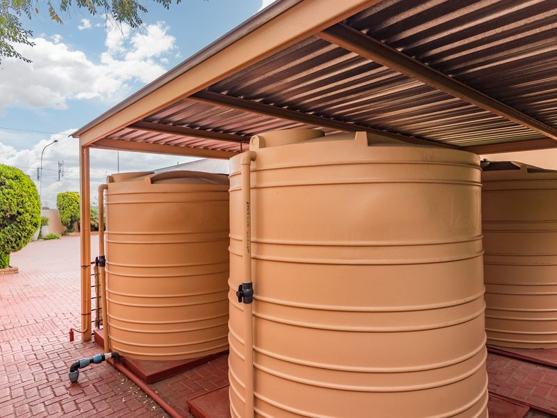 Outdoor utility area featuring multiple large water storage tanks protected by a corrugated metal roof structure on a paved surface.