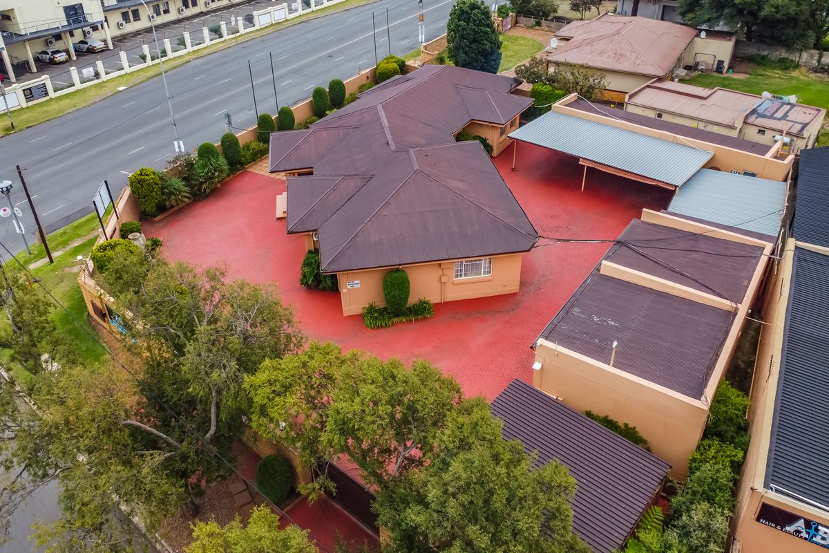 Aerial view of a commercial property featuring a main building with a metal roof, extensive paved parking area, and covered carport facilities.
