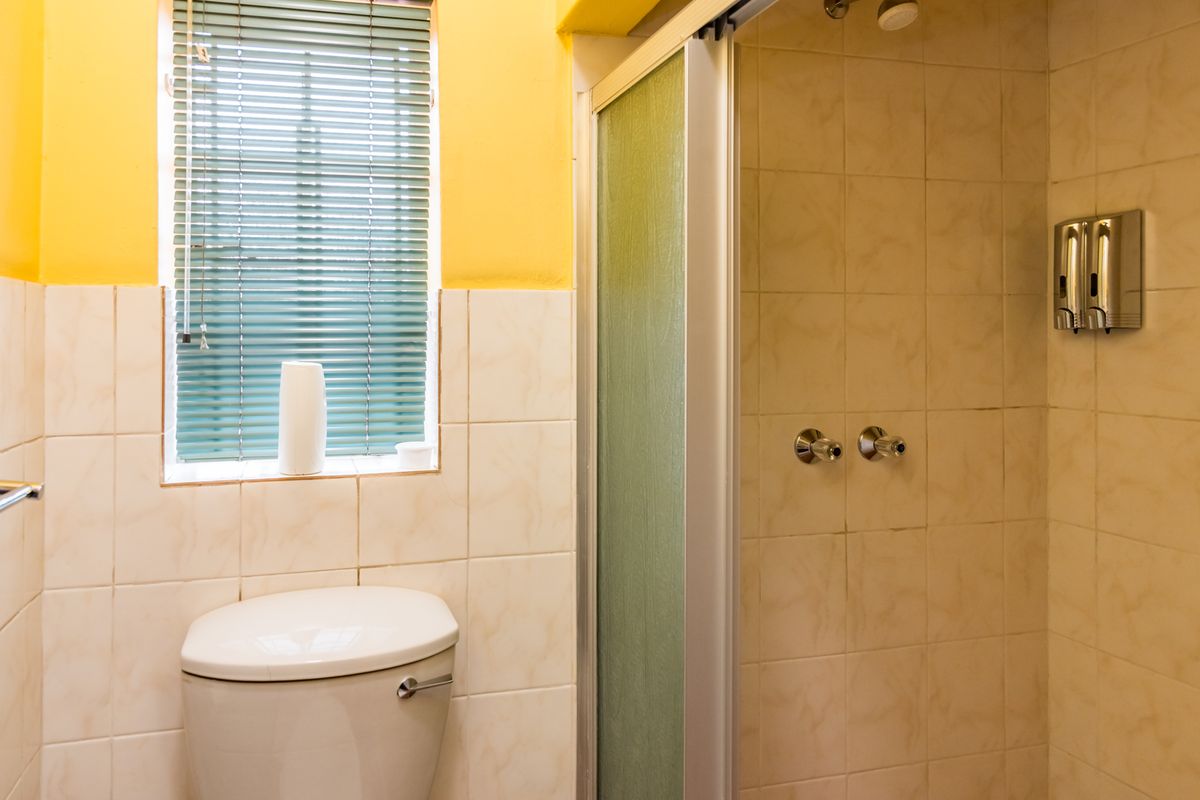 A functional bathroom featuring a shower enclosure, toilet, and tiled wall finishes with a window for natural light.