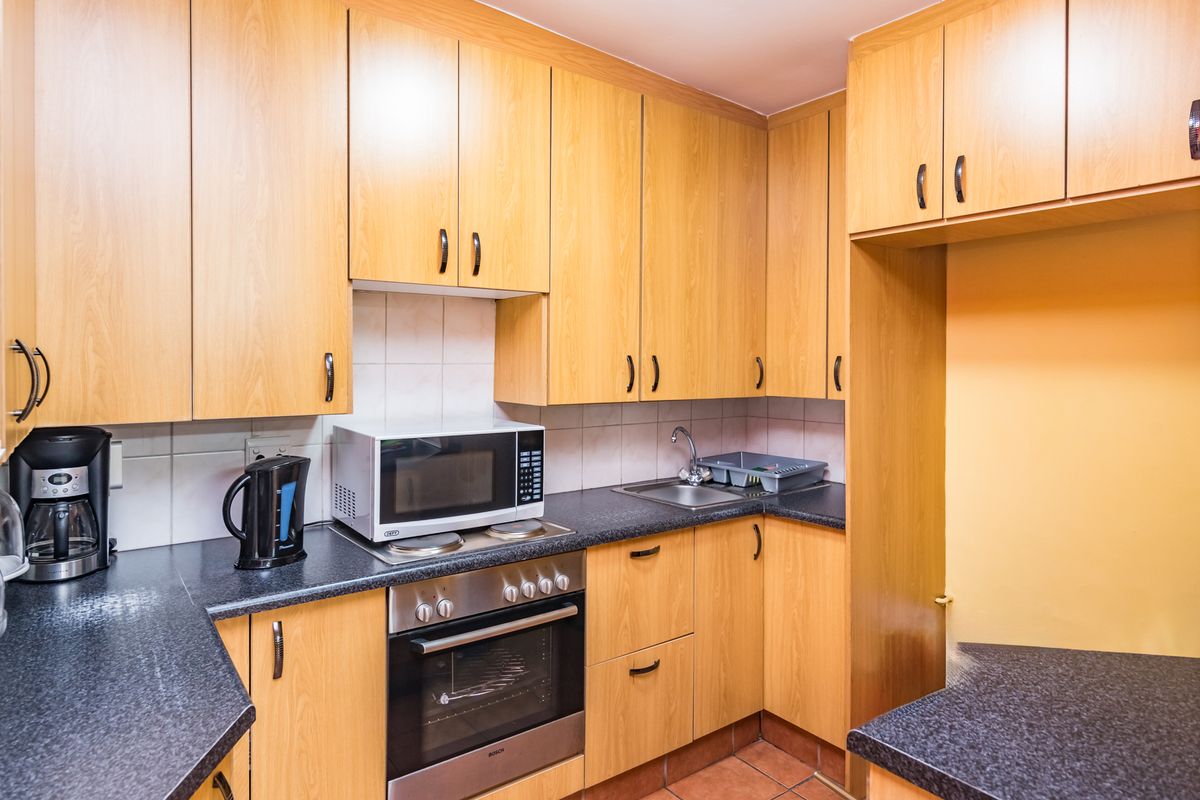 A functional kitchen featuring light wood-finish cabinetry, dark laminate countertops, a built-in oven, and tiled backsplash.