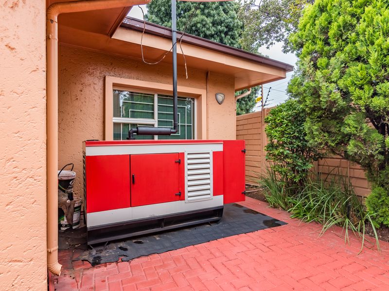 Exterior rear area featuring a large standby generator installed on brick paving, adjacent to the building wall and perimeter boundary.