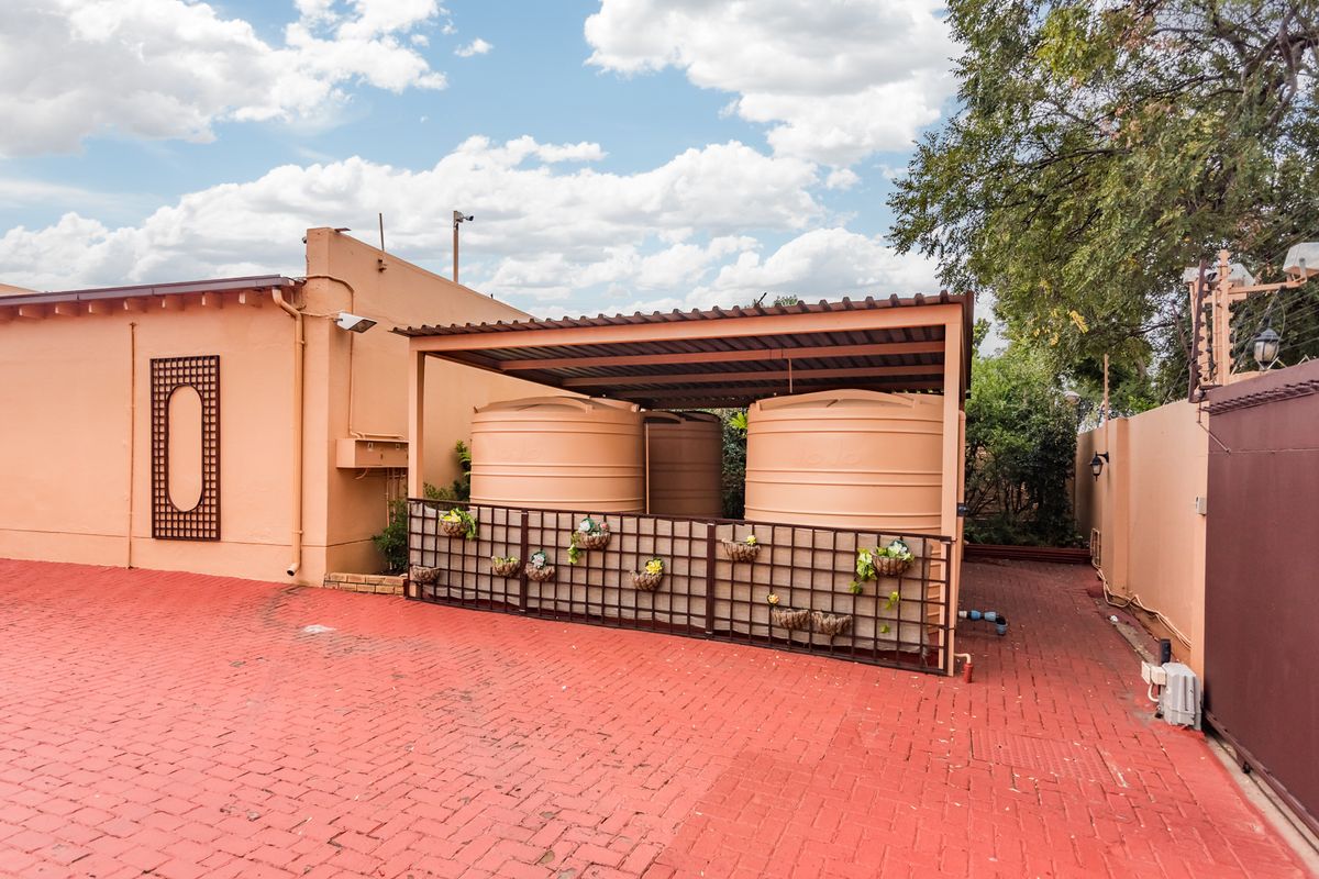 Rear exterior area featuring large water storage tanks under a covered structure, set on a paved driveway with perimeter security fencing.
