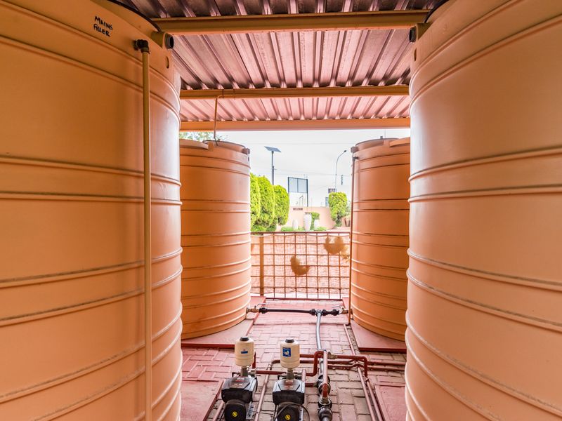 Utility area featuring multiple large water storage tanks and integrated pump systems with associated plumbing infrastructure under a covered structure.
