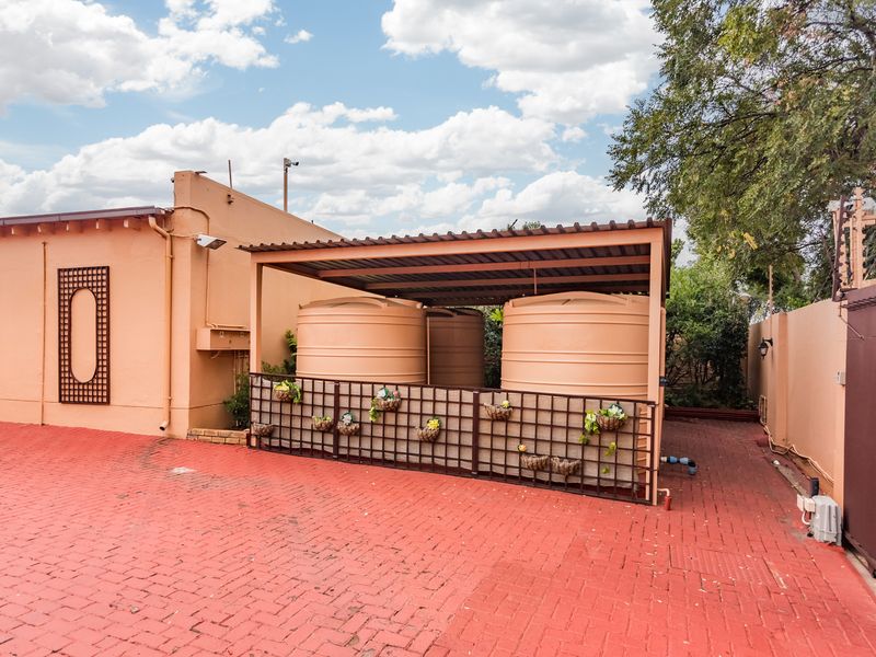 Rear exterior area featuring large water storage tanks under a covered structure, set on a paved driveway with perimeter security fencing.